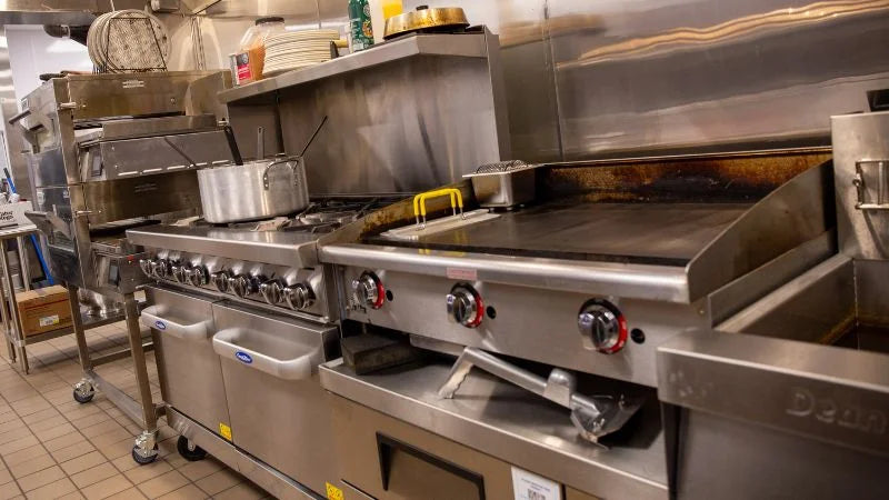 Commercial cook line with flat-top griddle, gas range, fryer, and stainless steel backsplash