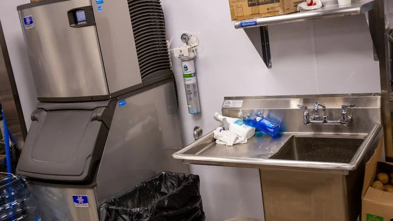 Ice machine and hand sink station with wall-mounted water filter in kitchen prep area