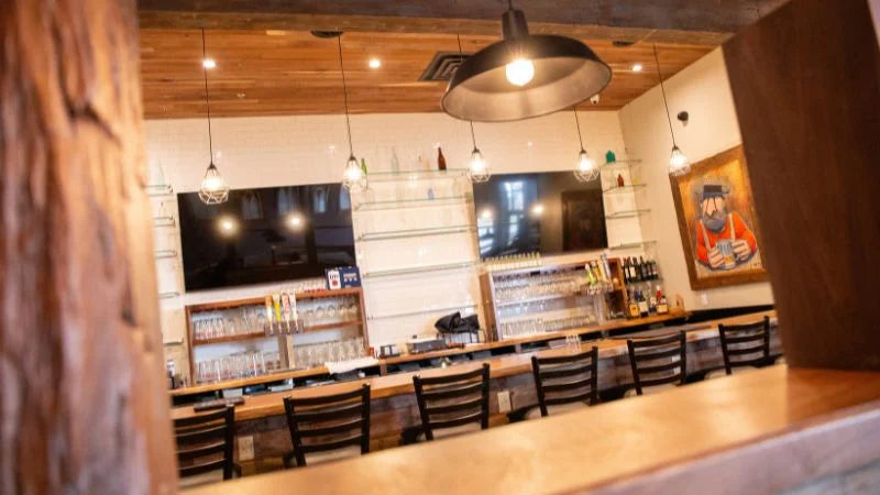 Restaurant bar interior with wood accents, pendant lighting, bar seating, and wall-mounted TVs