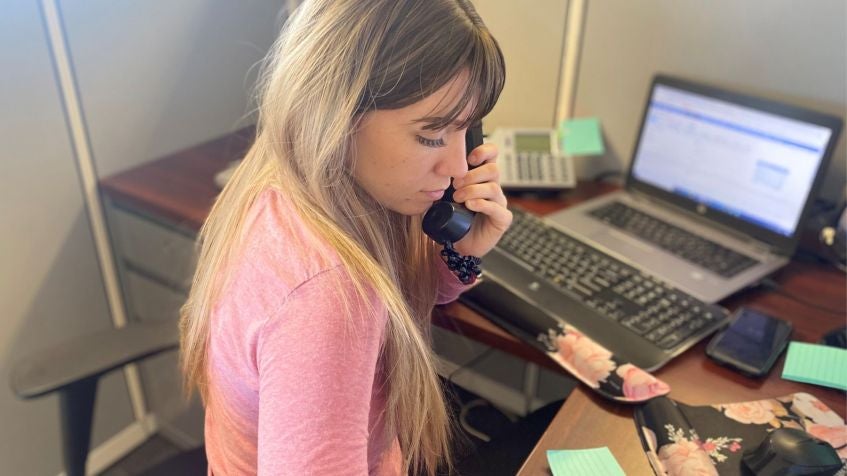 Office worker on phone at desk with laptop, handling customer support and order resupply tasks