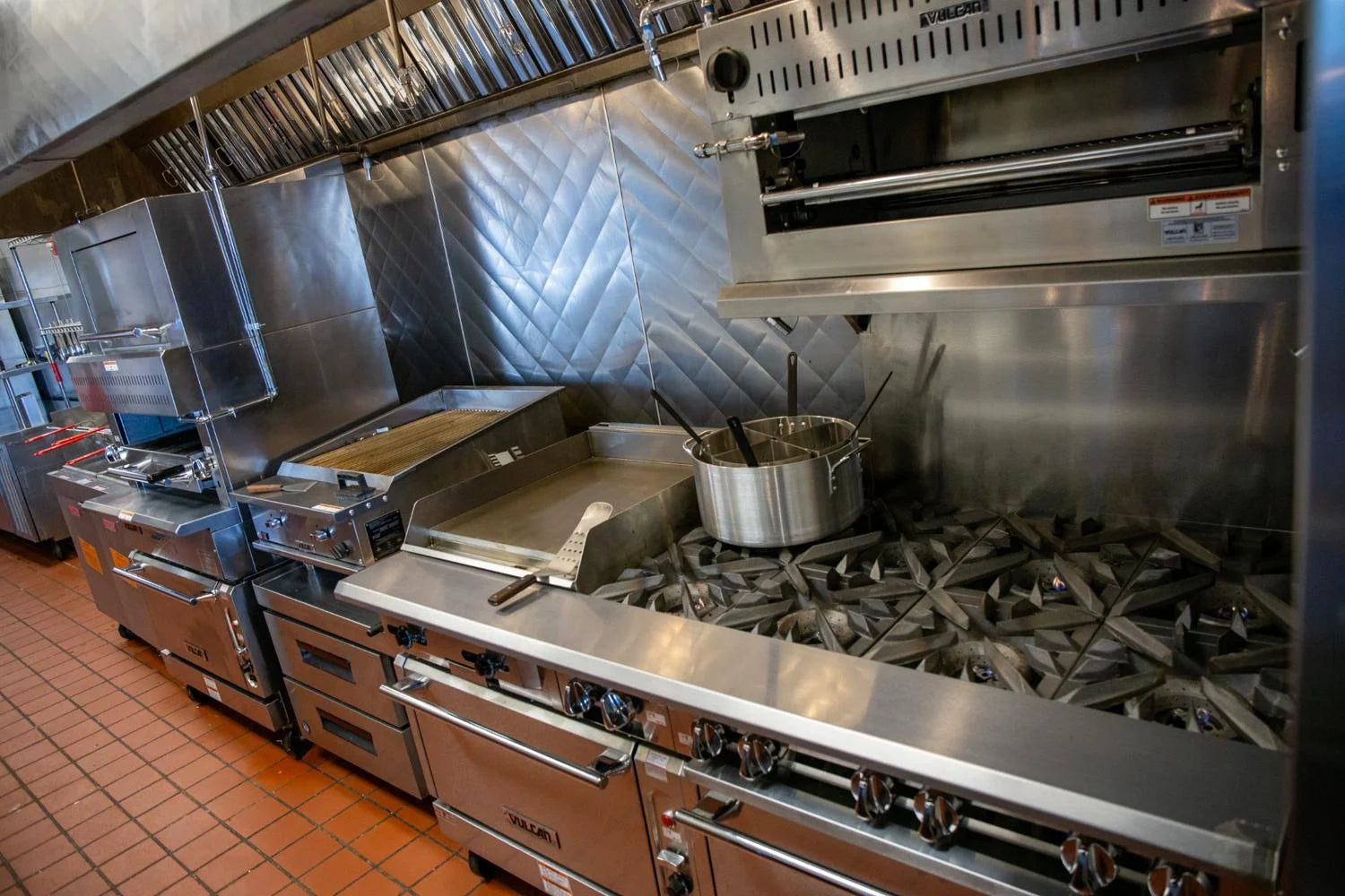 Stainless steel commercial kitchen equipment with burners and pots.