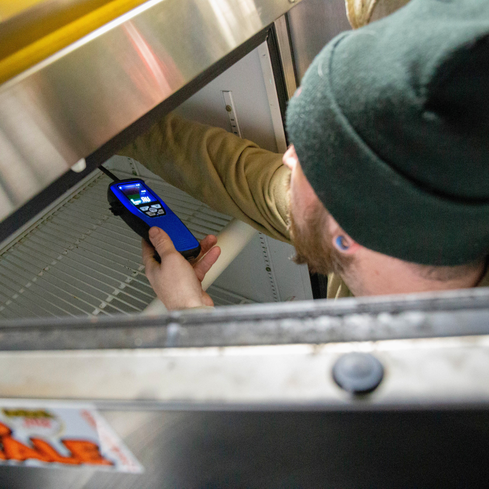 A technician using a digital multimeter to test the electrical components of a commercial refrigerator.