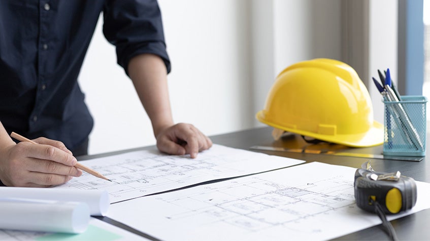 Reviewing construction plans with hard hat and tools on desk