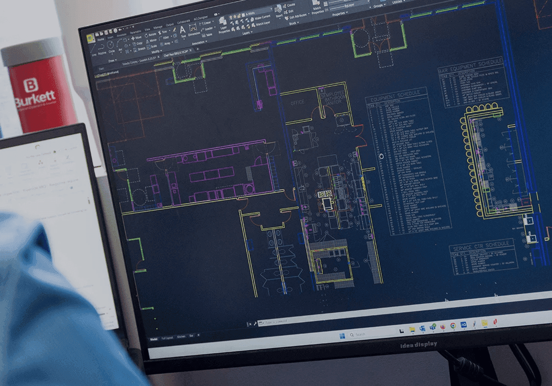 Computer screen displaying technical drawings with a blurred person wearing a blue shirt in the foreground.
